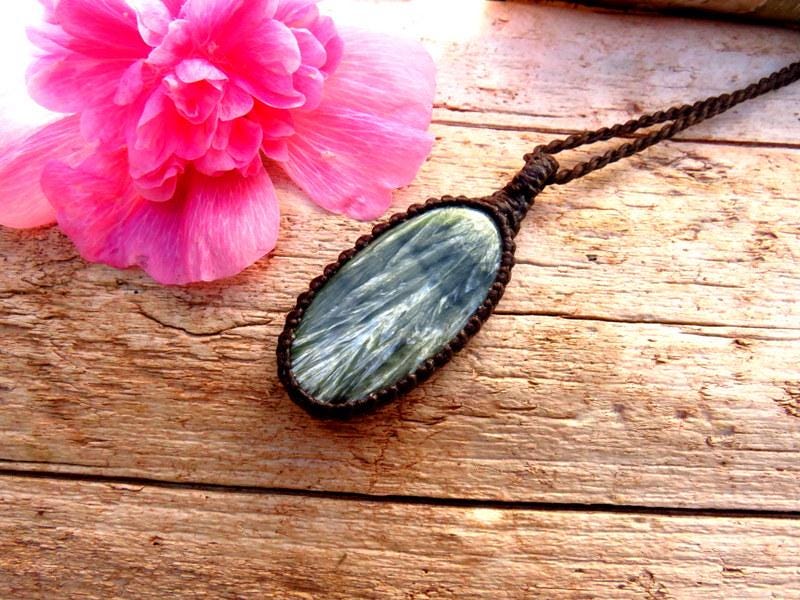May include: A green and white gemstone pendant with a brown cord necklace. The pendant is oval shaped and has a natural, organic look.